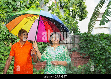 Felice amorevole coppia Senior in piedi sotto la pioggia con un ombrello avendo divertimento godere nel parco di tempo piovoso Foto Stock