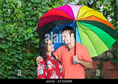 Felice coppia romantica in amore sotto l ombrello godendo la pioggia in-park sulla stagione estiva Foto Stock