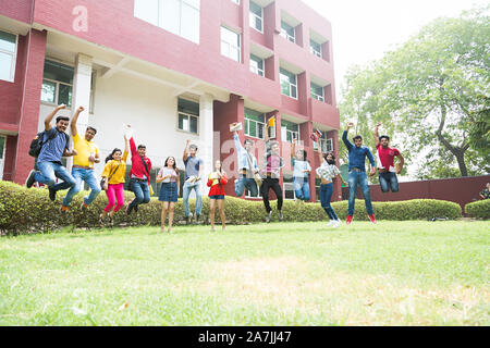 Un gruppo di giovani maschi e femmine studenti del college amici Jumping-up In-Outside Mid-Air edificio del campus Foto Stock