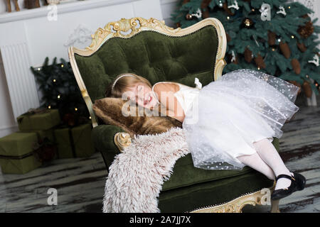 Bambina fingendo di essere dormire su una poltrona vicino a un albero di Natale per incontrare Santa quando egli porta presenta. Foto Stock