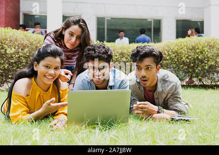 Scioccato Collegio quattro ragazzi e ragazze studenti amici Looking-At Laptop studiando l'E-Learning At-Campus Foto Stock