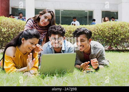 Quattro studenti del college amici Looking-At insieme allo schermo del laptop in chat In-Outside Campus Foto Stock