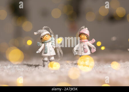Decorazione di Natale figurine a tema. Statuetta un ragazzo e una ragazza in maglia cappelli e sciarpe. Decorazione per albero di Natale. Decorazioni festive, calde luci bokeh di fondo Foto Stock