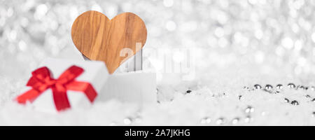 Confezione regalo con un nastro rosso e il cuore di legno nella neve con perle, testata Foto Stock