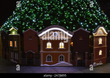 Albero di natale e piccole case sotto di esso nel centro della città di Burgas in Bulgaria. Decorazione di natale di notte. Foto Stock