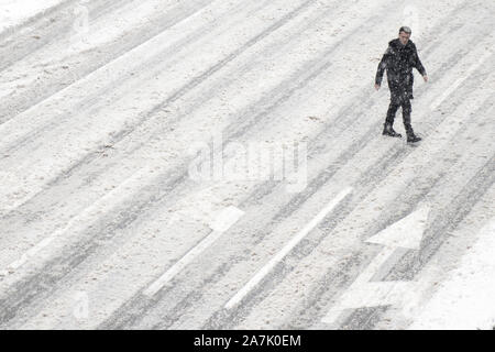 Belgrado, Serbia- 26 Gennaio 2019: Un uomo attraversare la strada al di fuori del crosswalk durante la tempesta di neve e di una vettura di pilotaggio, ad alto angolo di visione Foto Stock