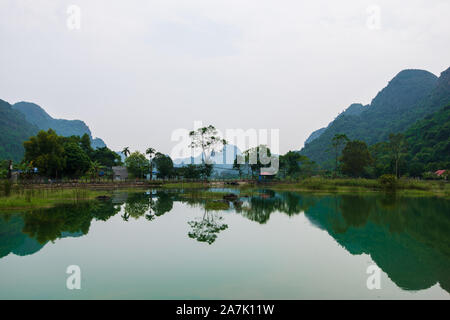 Le montagne si riflette in un'ember lago verde sull'hidden Cat Ba Island che viene regolarmente visitata da gite in barca intorno alla baia di Ha Long Foto Stock