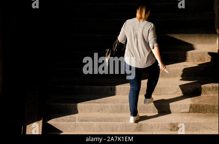 Uno più dimensione donna a piedi fino al pubblico le scale di luce e ombre, da dietro Foto Stock