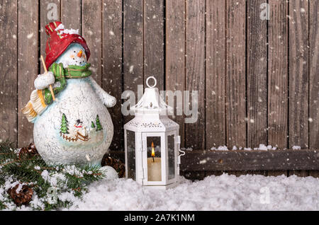 Natale pupazzo di neve e lanterna sulla neve contro un rustico in legno con sfondo spazio copia Foto Stock