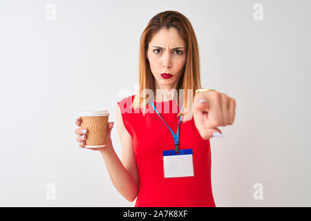 Redhead imprenditrice indossando la scheda id bere tazza di caffè isolato su sfondo bianco puntando con il dito per la telecamera e a voi, mano segno, Foto Stock