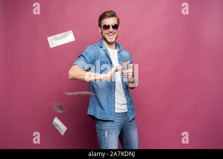 Concetto di ricchezza finanziaria, di prosperità e di vincite alle lotterie - Uomo gettando via il suo denaro isolato su rosa Foto Stock