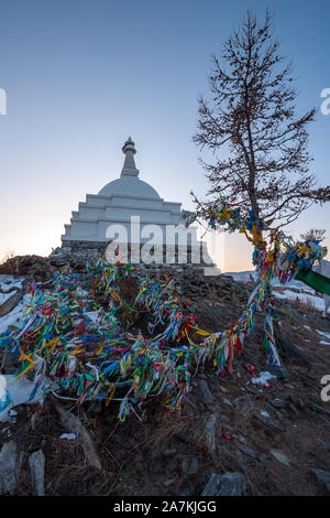 Stupa buddisti sull isola di Ogoy sul lago Baikal con un albero e molti appeso bandiere colorate. In inverno, la neve sulla terra. Di sera. Foto Stock