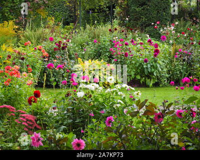 Avvicinando autunno a Chenies Manor garden. Il sunken garden wth colorate varietà dahlia, hosta con foglie rosso, rosa,fioriture di viola e il percorso. Foto Stock