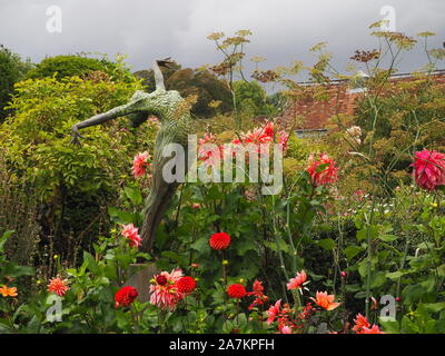 Tarda Estate dalie in piena fioritura a Chenies Manor giardino.JA Jonathan Hateley scultura raggiunge fino oltre il colore arancione pallido blumi di Dahlia labirinto. Foto Stock