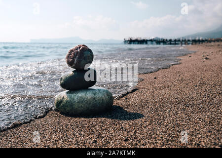 Pila di pietre zen sulla spiaggia vicino al mare. Torre di spa rocce sulla sabbia a Ocean. Ciottoli equilibrato all'aperto sulla soleggiata giornata estiva. Oriental calma ed armonia s Foto Stock