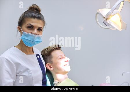 Teen boy in visita dal dentista seduto in poltrona, giovane donna medico curante denti Foto Stock