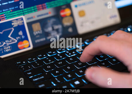 Una mano digitando su una tastiera con lo schermo di un computer e le carte di credito in background. Concetto: frodi utilizzando il furto di carte di credito per effettuare il pagamento on-line Foto Stock