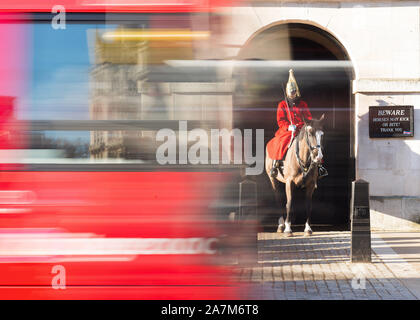 Un rosso London bus passando un membro del Queen's Life Guard nel manto scarlatto al di fuori delle Guardie a Cavallo, Whitehall. Fotografato con una bassa velocità dell'otturatore. Foto Stock