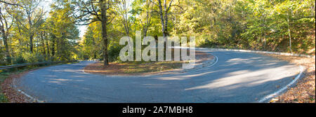 Una tortuosa strada curva attraverso gli alberi d'autunno. Panorama Foto Stock