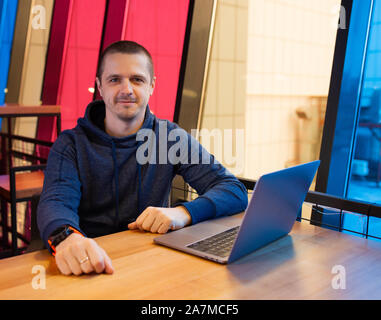 Uomo in felpa con cappuccio seduti alla scrivania con computer portatile Foto Stock