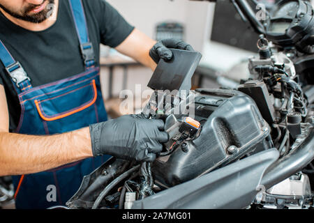 Elettricista o aggiustatore a guanti di protezione del cablaggio di collegamento in motocicletta durante una riparazione in officina Foto Stock