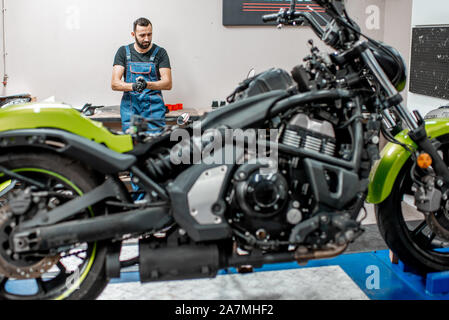 Ritratto di un ciclista o aggiustatore in tute da lavoro in piedi vicino alla moto durante la riparazione in officina Foto Stock