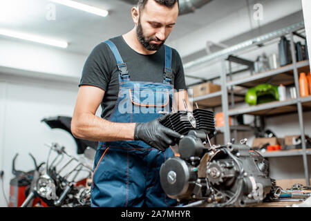 Operaio in tuta smontaggio motore del motociclo durante una riparazione presso il tavolo di lavoro del workshop Foto Stock