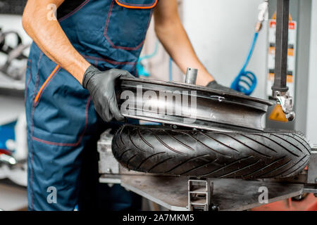 Lavoratore di servizio cambio pneumatici moto su un equipaggiamento speciale per l'installazione di pneumatici in officina, vista da vicino Foto Stock