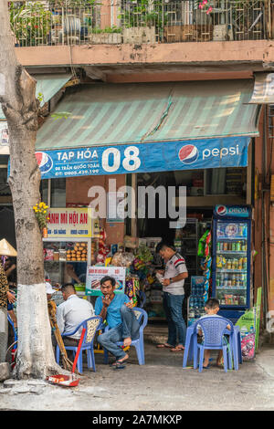 Da Nang, Vietnam - Marzo 10, 2019: centro storico quartiere urbano scena. Gli uomini seduti a colazione nella parte anteriore del piccolo negozio conveniente sotto Peps Foto Stock