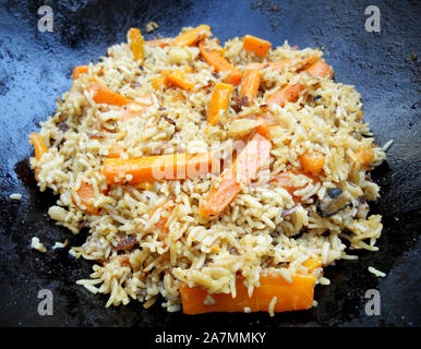 Ghisa ciotola pilaf, ampia piastra nera viene riempito con vari fatti in casa funghi Riso, giallo carota, aglio bianco plov vegetali. Pilaf set composto o Foto Stock