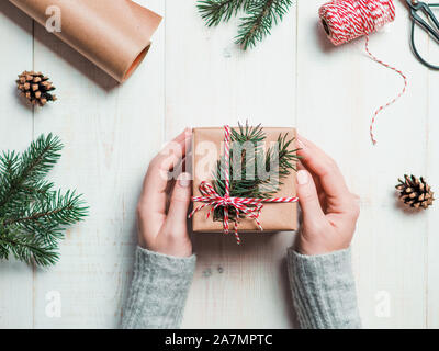 Regalo di Natale sfondo incarto.mani femminili tenendo presente il natale Scatola avvolto in kraft, vista dall'alto. Vacanze invernali concetto, piatto lay.Donna con rosa pastello manicure opaca di imballaggio regalo di Natale Foto Stock