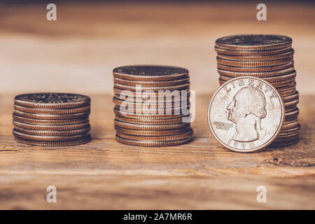 Primo piano di tre quarti americano di pile con una moneta dal lato della faccia in piedi contro la pila più alta. Il libero commercio, economia, il liberalismo, il capitalismo Foto Stock