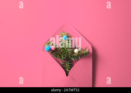 Busta rosa con abete rami e baubles su sfondo rosa. minimo composizione di natale. busta di artigianato e di Natale rami d abete. la piana Foto Stock
