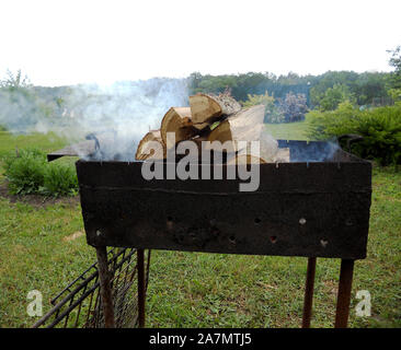 Bel rosso fuoco dal legno di fetta, grigio scuro nero all'interno di carboni braciere in metallo. La combustione del legno nel braciere sul colore giallo brillante fuoco. Le fiamme incendi preparata Foto Stock
