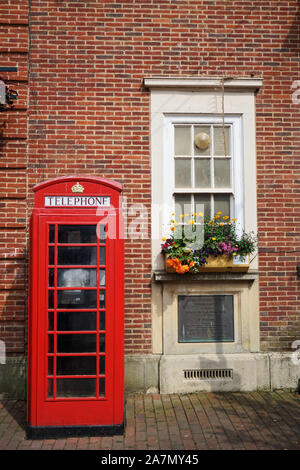 Iconico telefono rosso britannico di fronte a un edificio in mattoni con finestra e scatola di fiori in una giornata luminosa e soleggiata, Sidmouth, Devon, Regno Unito Foto Stock