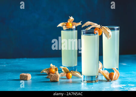 Cocktail alcolico con ouzo greco acquavite di anice o arabo alcool bere raki in vetro highball, decorate Physalis peruviana e lo zucchero di canna nel blu c Foto Stock