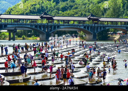 I visitatori un tuffo per rinfrescarsi in acqua in una posizione nota per il pesce in scala barriere sagomati che formano piccole cascate nel quartiere Fuyang, Hangzhou ci Foto Stock