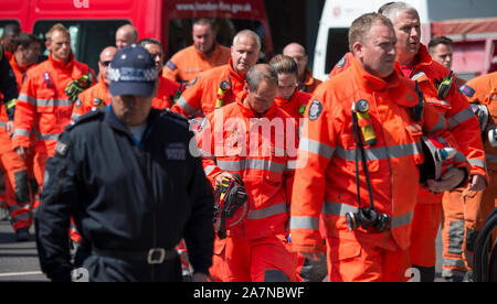 I vigili del fuoco e i membri della ricerca e salvataggio in aree urbane team pausa per un attimo di silenzio prima di continuare la ricerca di vittime nei resti della torre Grenfell disastro incendio nel Nord di Kensington, West London. Il fuoco era la più letale Fuoco nazionale dopo la seconda guerra mondiale. L'incendio scoppiato nell'24 piani di blocco di appartamenti appena prima di 1:00am il 14 giugno 2017, causando 72 morti e il ferimento di più di 70 persone. Foto Stock