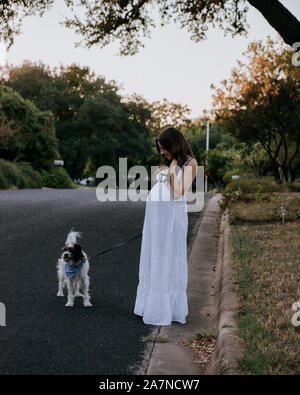 Donna incinta abito bianco a piedi il suo cane Foto Stock