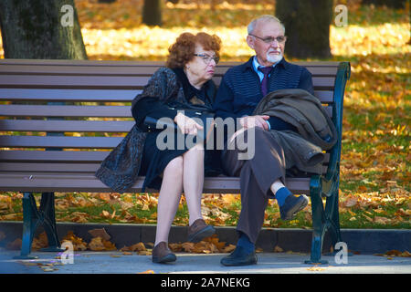 Kharkiv, Ucraina - 14 Ottobre 2019: Elegante coppia di anziani seduti su una panchina nel parco di autunno Foto Stock