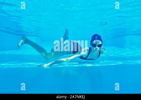Ragazza adolescente in costume da bagno con gli occhiali e cuffia per la piscina di nuoto sott'acqua in piscina