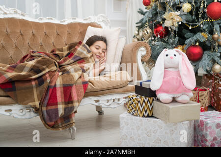 Credo ai miracoli. Momento magico. La notte di Natale. Felice anno nuovo. Bambina lettino dormire vicino a albero di natale classici interni. Vacanza in famiglia. Albero di Natale e regali. Sognare di doni. Foto Stock