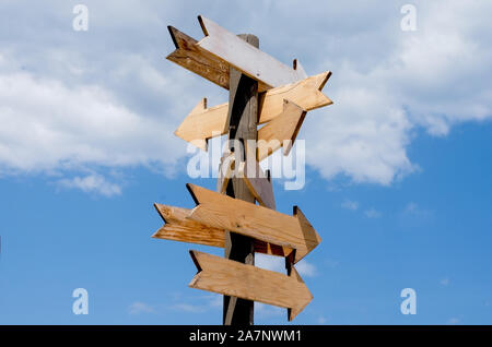 Più bianco freccia in legno indicazioni sul palo di legno contro il cielo blu . Foto Stock