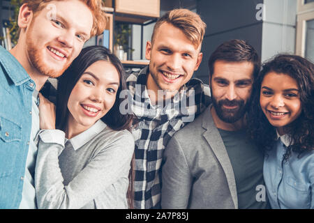Startupers lavorando insieme a Office abbracciando permanente tenendo selfie foto allegro close-up Foto Stock
