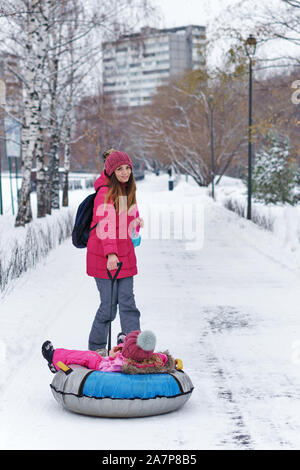 Attivo giovane madre rotoli il suo bambino su un snow tubing. Attività invernali. La Felicità di essere un genitore. Aspetto familiare. Foto Stock