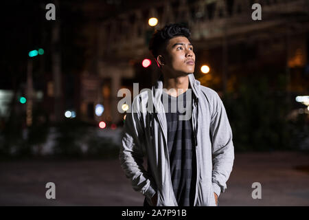 Giovane uomo asiatico pensando per le strade della città di notte Foto Stock