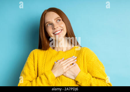 Ritratto di bella grato redhead caucasian donna con sorriso affascinante mantenendo entrambe le mani sul cuore , esprimendo gratitudine, sensazione di amore, dreami Foto Stock