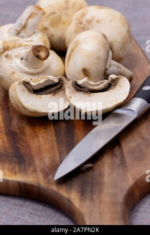 Closed Cup funghi bianco su un tagliere di legno. Su una tovaglia di colore grigio Foto Stock