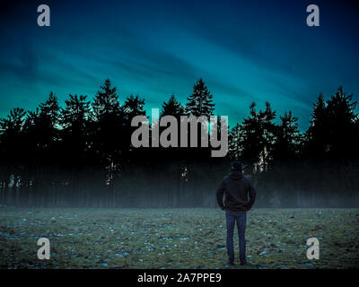 Uomo a camminare da sola nel buio magico foggy selvaggio paesaggio forestale. Foto Stock