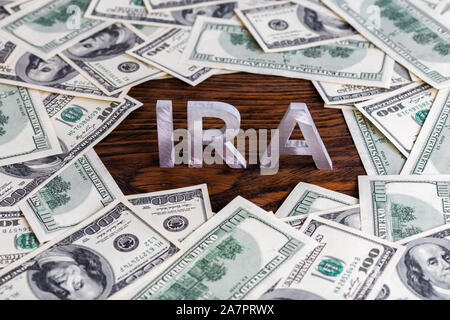 La parola ira singoli conto pensione fatta di metallo argento lettere sullo sfondo di legno circondato da US dollar banconote Foto Stock